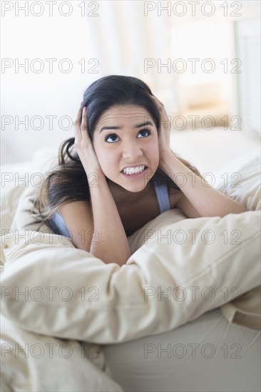 Frustrated Hispanic woman covering ears in bed