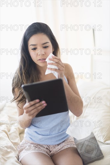 Hispanic woman holding tissue and using digital tablet in bed