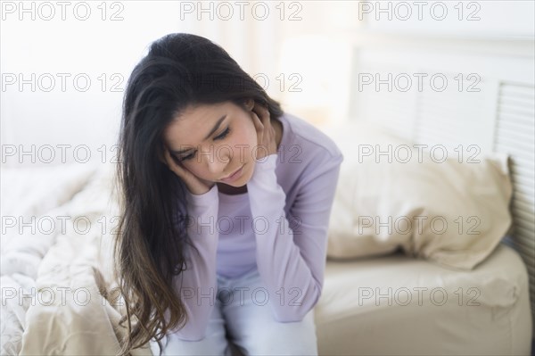 Sad Hispanic woman sitting at edge of bed