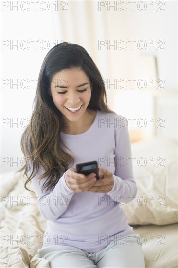 Happy Hispanic woman text messaging in bed