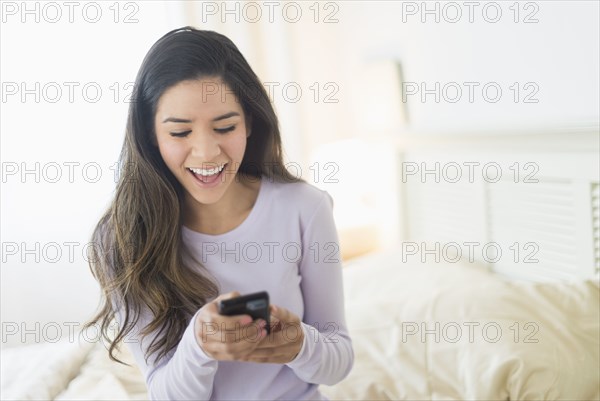 Happy Hispanic woman text messaging in bed