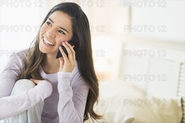 Happy Hispanic woman talking on cell phone in bed