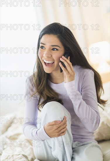 Enthusiastic Hispanic woman talking on cell phone in bed