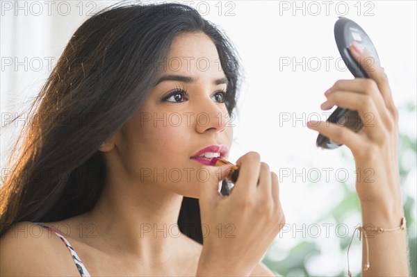 Hispanic woman applying lipstick in compact mirror