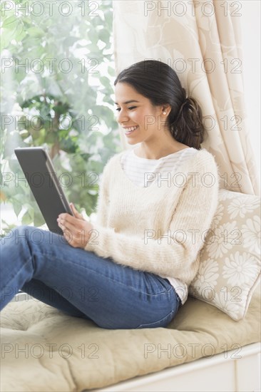 Hispanic woman using digital tablet at window seat