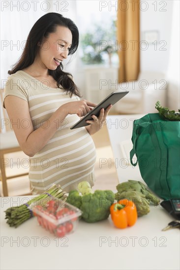 Pregnant Japanese woman using digital tablet in kitchen