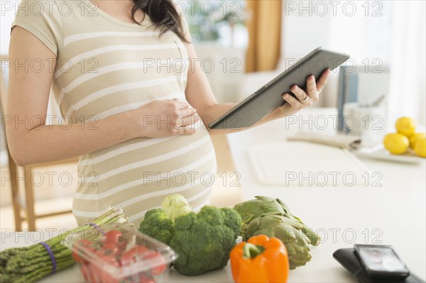 Pregnant Japanese woman using digital tablet in kitchen