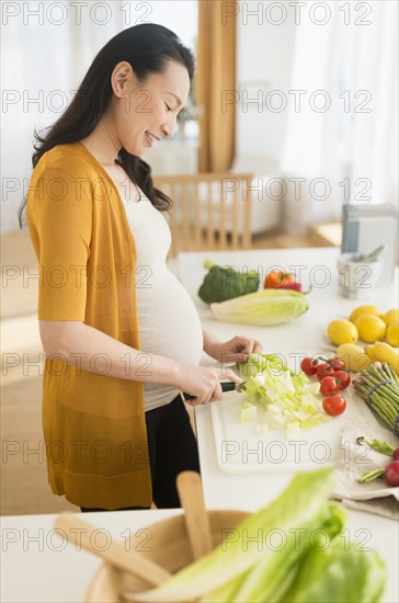 Pregnant Japanese woman slicing vegetables in kitchen