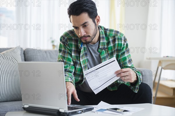 Mixed race man paying bills in living room