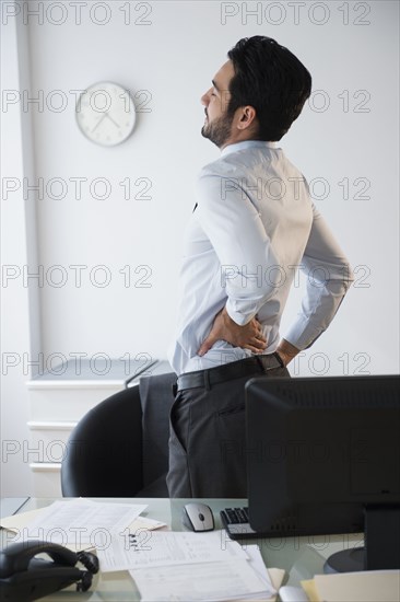 Mixed race businessman rubbing his back in office