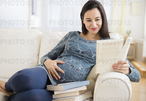 Pregnant Caucasian woman reading baby books on sofa