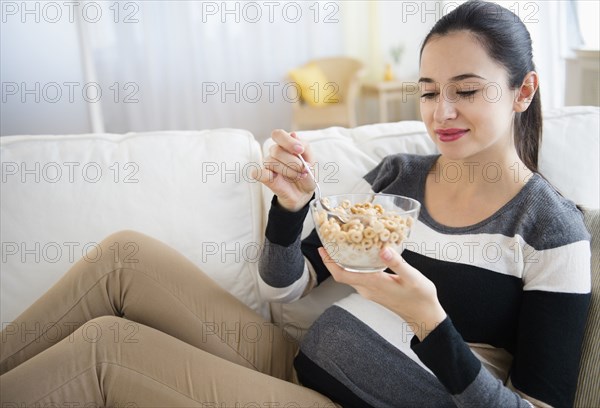 Pregnant Caucasian woman eating on sofa