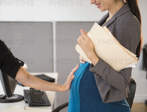 Pregnant Caucasian businesswoman showing off belly in office