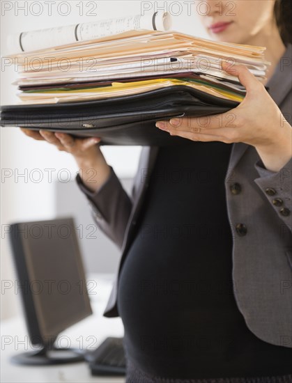 Pregnant Caucasian businesswoman carrying folders in office