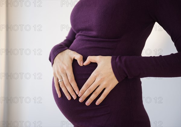 Pregnant Caucasian woman making heart shape on belly