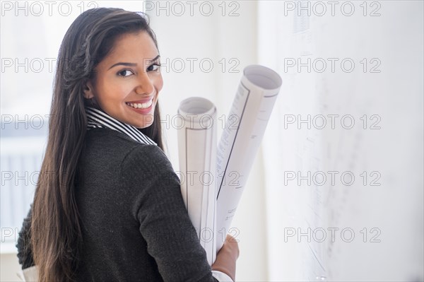 Hispanic architect carrying blueprints in office