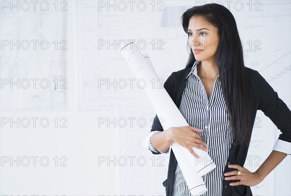 Hispanic architect carrying blueprints in office