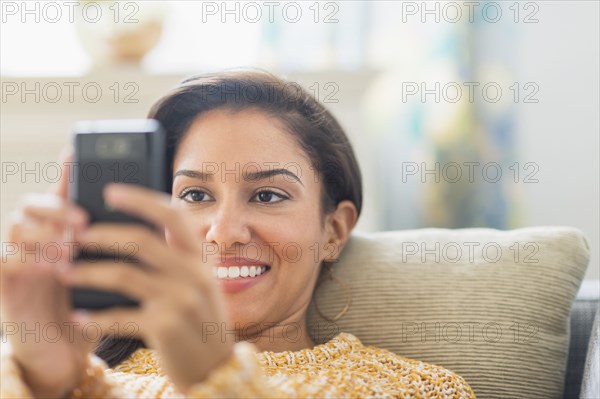 Hispanic woman using cell phone on sofa