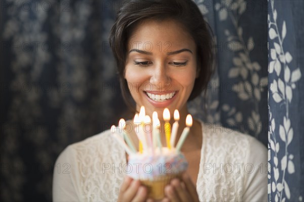 Hispanic woman looking down at lit candles on birthday cupcake