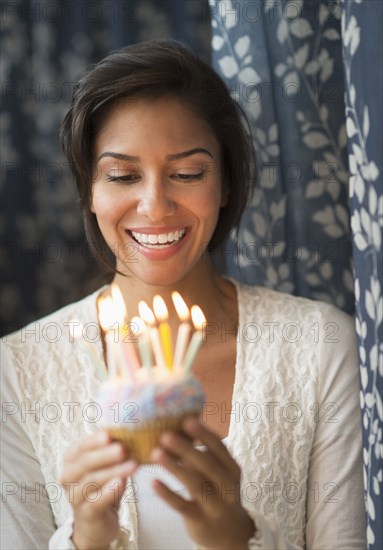 Hispanic woman looking down at lit candles on birthday cupcake