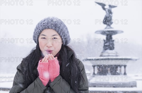 Asian woman blowing on hands in snow