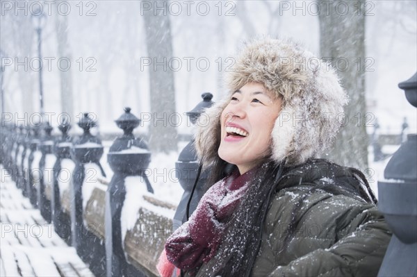 Asian woman sitting on park bench in snow