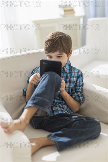 Hispanic boy using digital tablet in armchair