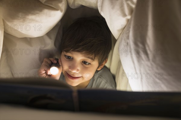 Hispanic boy reading under covers