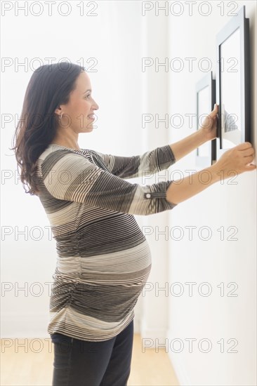 Pregnant Hispanic woman hanging pictures