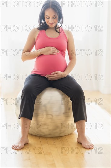 Pregnant Hispanic woman sitting on fitness ball