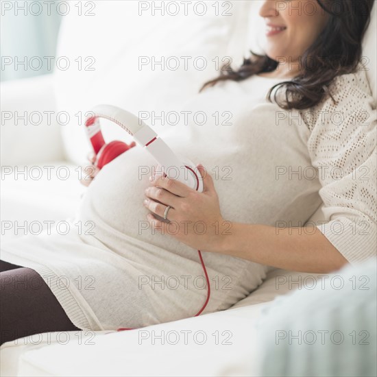 Pregnant Hispanic woman holding headphones on belly