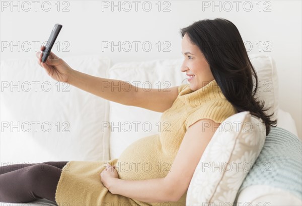 Pregnant Hispanic woman taking picture with cell phone