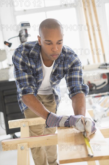 Black carpenter measuring wood in shop