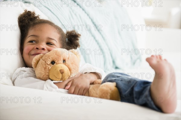 Black girl hugging teddy bear on sofa