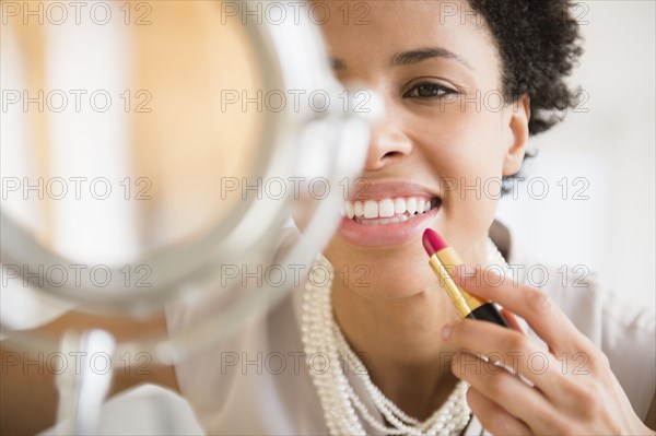 Black woman applying makeup in mirror
