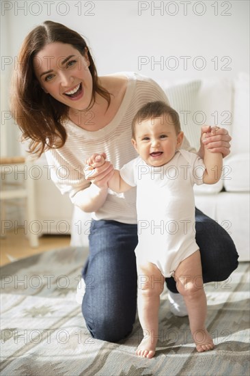 Mother helping baby stand in living room