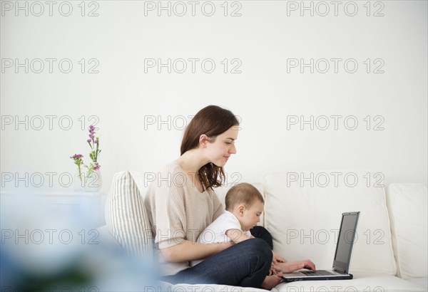 Mother and baby using laptop on sofa