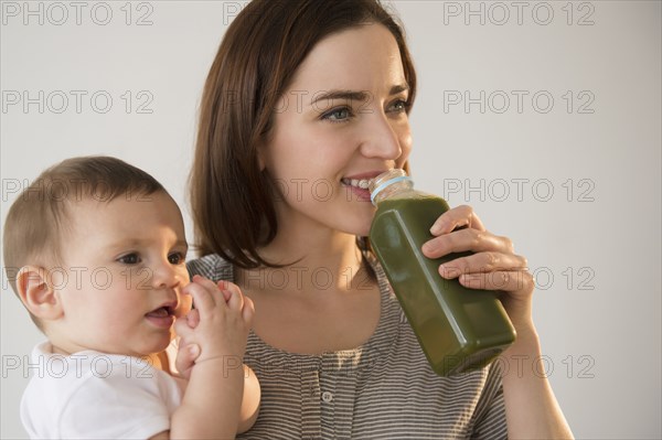 Mother holding baby and drinking green juice