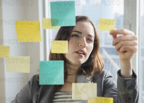 Businesswoman reading sticky notes on glass