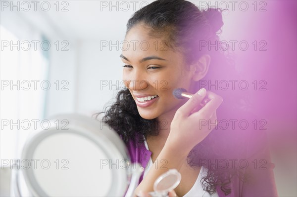 Mixed race woman applying makeup in mirror