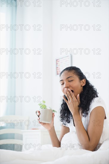 Tired mixed race woman drinking coffee in bed