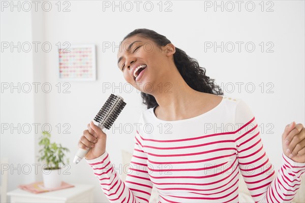 Mixed race woman singing into hairbrush