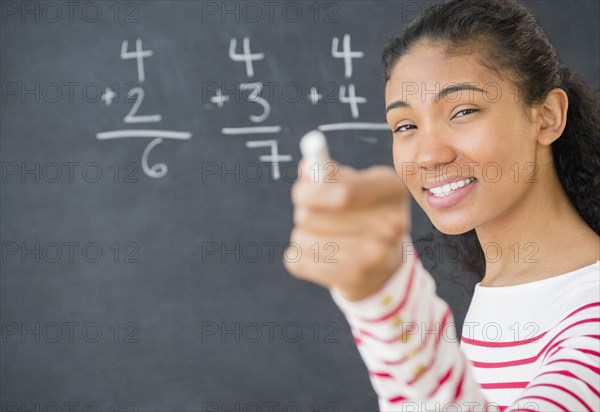 Mixed race teacher doing math on chalkboard