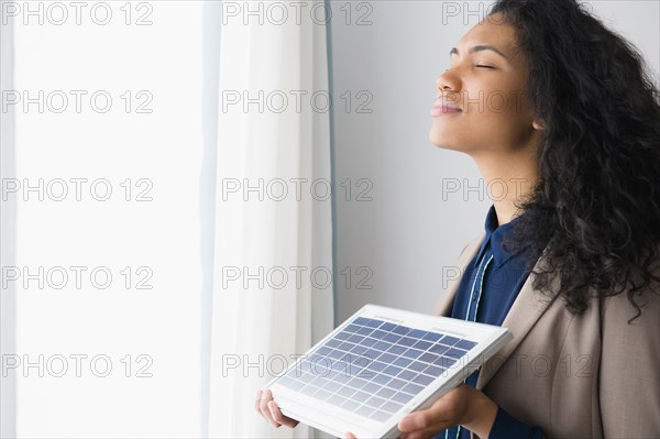 Mixed race woman holding solar panel by window