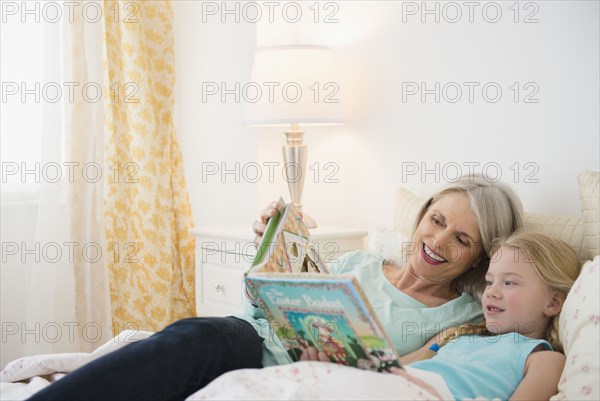 Senior Caucasian woman and granddaughter reading in bed