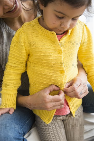 Hispanic mother buttoning daughter's sweater