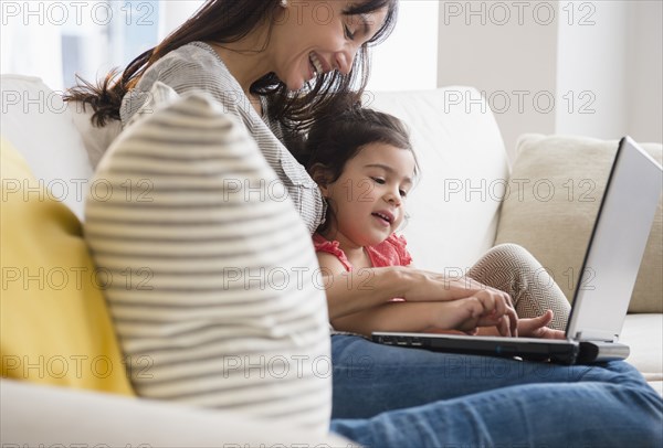 Hispanic mother and daughter using laptop on sofa