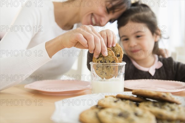 Hispanic mother and daughter dunking cookies in milk
