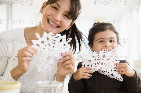 Hispanic mother and daughter making paper snowflakes