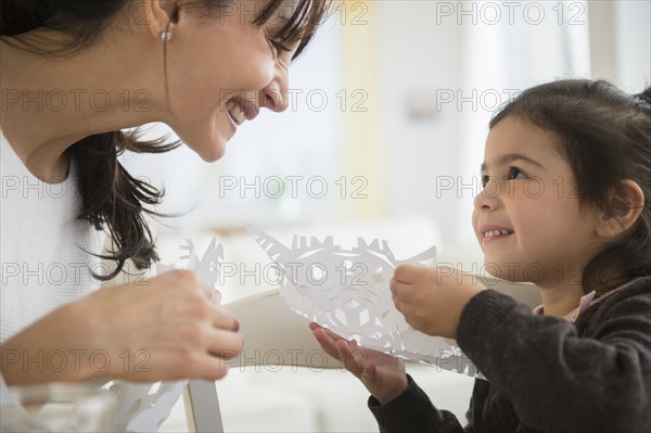 Hispanic mother and daughter making paper snowflakes